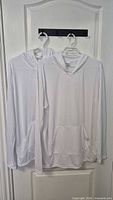 Front view of both white Gildan Performance hoodies hanging side by side