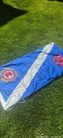 Full view of flag laid out on grass showing crest, white stripe, red rose