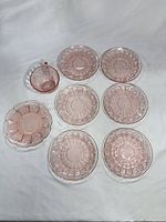 Eight pink depression glass pieces arranged on white backdrop