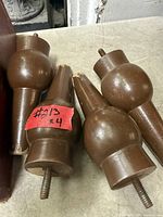 Set of four brown wood screw-on legs with threaded studs, showing wear and chips