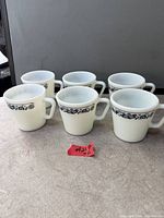 Six matching white Pyrex mugs with blue floral band