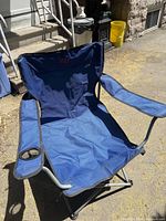 Full view of blue folding camping chair showing fabric, armrests, cup holder, and metal frame