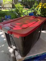 Angled view of the tote showing black body, red lid, grey latch