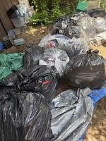 Multiple black contractor bags filled with clothing lying on tarps outdoors