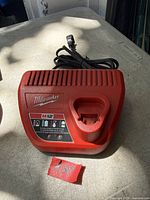 Top view of Milwaukee M12 battery charger showing logo, LED indicators, cord, and battery slot