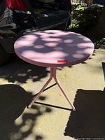Full view of pink round metal patio table on driveway