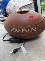 Closed football-shaped cooker showing brand name and cord