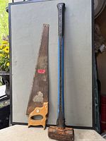 Hand saw and sledgehammer standing upright for full view