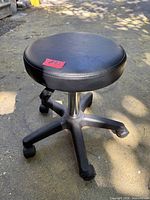 Full view of black adjustable stool showing round seat, chrome post, five-spoke base with casters
