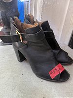 side view of both black leather ankle booties showing open toe, strap, heel and size tag