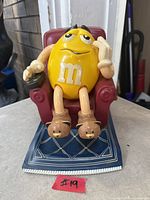 Full view of yellow M&M candy dispenser in chair on base