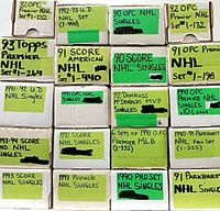 Front view of stacked white cardboard card boxes labelled with brands and sports