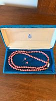 Pink beaded necklace and stud earrings in blue case
