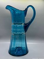 Full side view of blue art glass pitcher showing handle, spout, enamel decoration