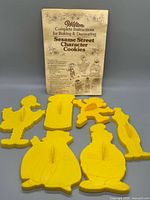 Front view of all six yellow Sesame Street cookie cutters with instruction booklet behind