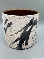 Front view showing textured white glaze with black abstract splatter and brown interior