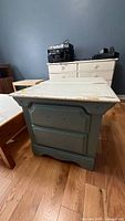 Angled view showing blue-green nightstand with white top, missing hardware, chipped paint