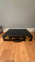 Closed black briefcase on floor, showing top handle and locks