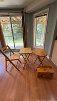 Wood folding chair beside square and round folding tray tables and decorative storage box
