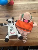 Front view of cow plush with sign and pig plush in toga