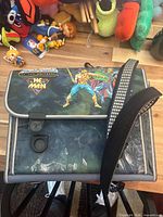 Front view showing He-Man and Skeletor artwork, latch closures, shoulder strap