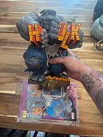 Front view of Grey Hulk statue held in hand above comic poster