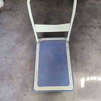 Top view of dolly showing metal frame, rubber deck, edge bumper, handle upright