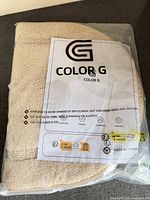 Packaged beige oval bath mat showing Color G branding and sealed bag