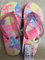 Top view of flip flops showing multicolor footbed, straps, hanger, and size tag