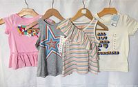 Four tops hanging to show fronts, colours, graphics, tags visible