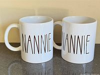 Front view of both white ceramic mugs showing NANNIE text