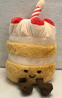 Front view of strawberry birthday cake plush showing face, layers, strawberries, candle, legs