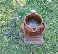 Overall view of rusted Hilts electric melting pot with power cord on grass