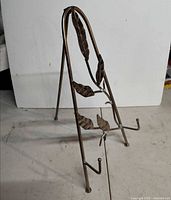 Front angle of metal easel showing leaf decoration and support hooks