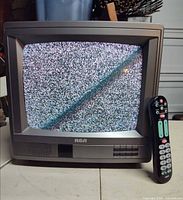 Front view of RCA CRT TV powered on showing static with remote beside