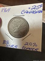 Obverse or reverse view of 1964 Canadian quarter in cardboard flip showing caribou design and handwritten composition