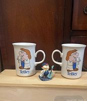Front view of two Tetley mugs and Clarence figurine