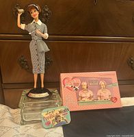 Barbie doll on stand beside sealed chocolate box and mint tin