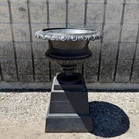 Full view of cast iron urn on pedestal outdoors