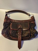 Front view showing metallic brown body, brown leather trim, buckle front pocket, hardware