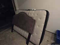 Mattress front showing tufted top and upholstered headboard leaning against it