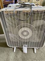 Front view of white box fan showing grille and support feet