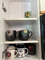 Cabinet view showing striped monogram mug, three floral mugs on middle shelf, multiple mugs on bottom shelf