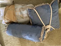 Three pillows, two blue jacquard with cord trim (rectangular, bolster) and portion of gold/gray jacquard piece