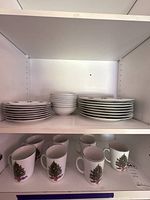 Stacks of dinnerware on cabinet shelves showing plates, one bowl, and mugs