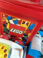 Red LEGO tub packed with bricks beside Fisher-Price Chatter Telephone and glimpse of blue plastic train case
