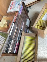 Rack of assorted jewel-case CDs beside two cartons of yellow-spine duplicates