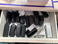 Drawer containing multiple black, silver and textured eyeglass cases with two frames visible