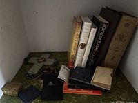 Shelf with upright hardcover books, wall cross, rosary, small boxes and pocket books