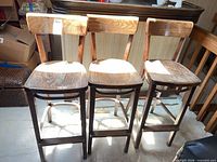 Three dark brown wooden bar stools side by side